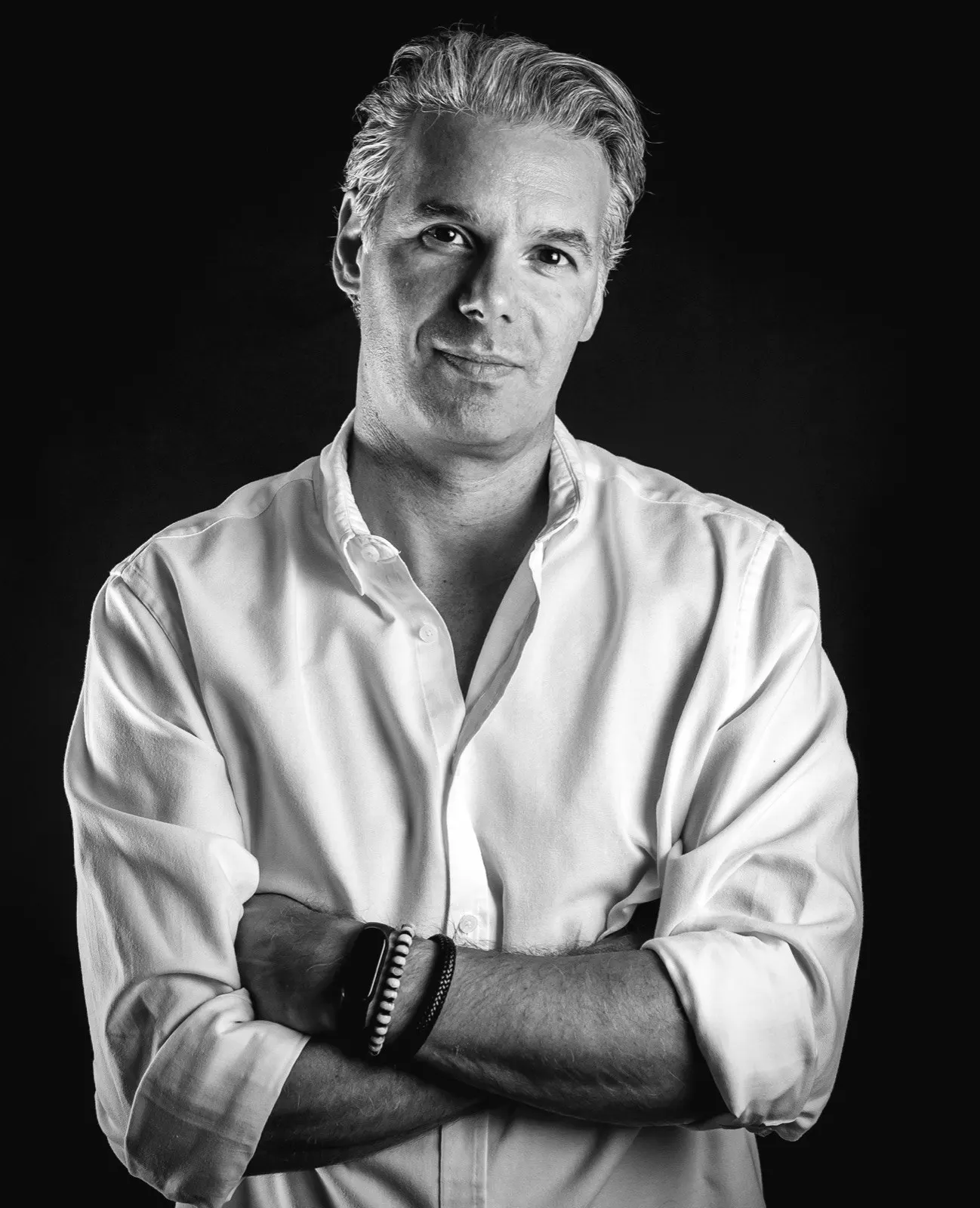 Ritratto in bianco e nero di Michele Stival: camicia bianca, braccia incrociate, fondo nero